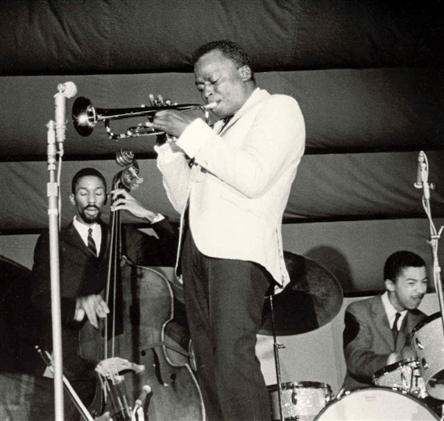 Miles Davis playing trumpet on stage with his second quintet|