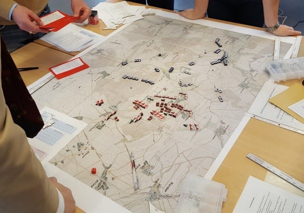 A group of people standing around a large table covered with a map and game pieces.