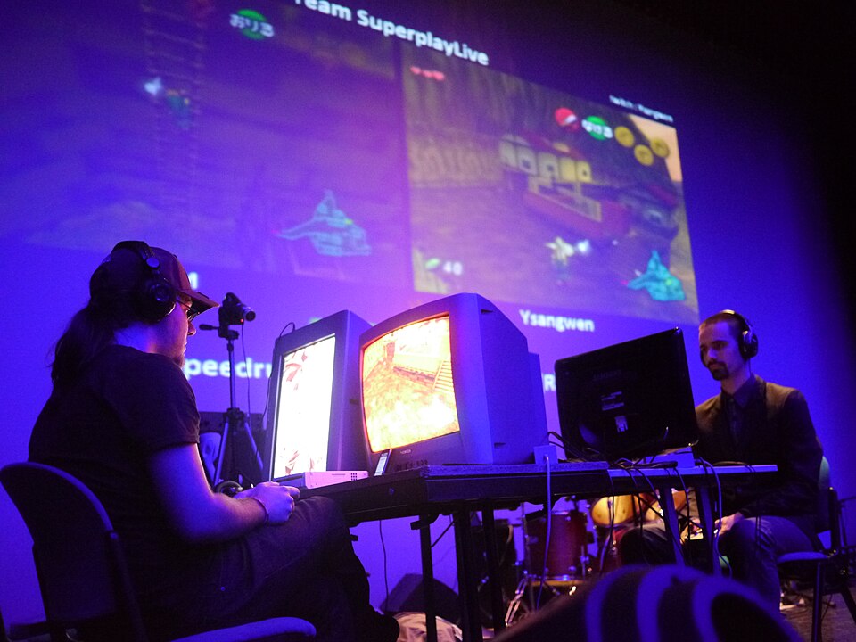 A person seated at a console playing a video game before a screen at a gaming convention.