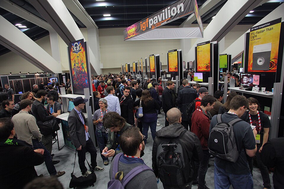 Wide view of a crowded conference expo floor with booths showing independent games