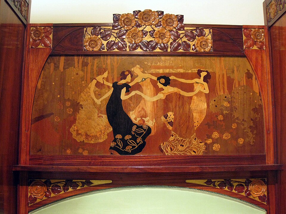 Inlaid wood marquetry panel depicting figures dancing in flowing decorative style.