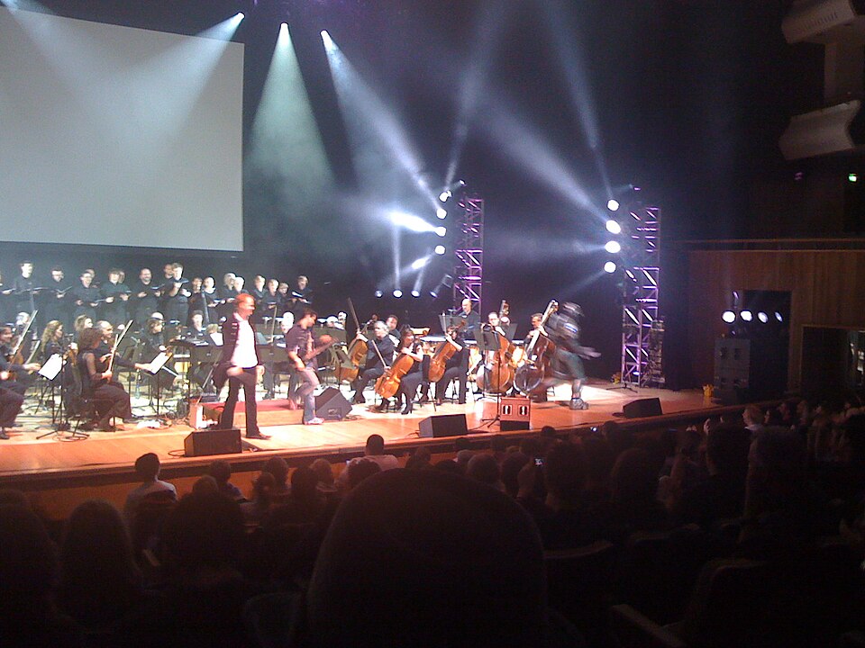 A symphony orchestra on a concert-hall stage beneath a large video screen during a Video Games Live performance.