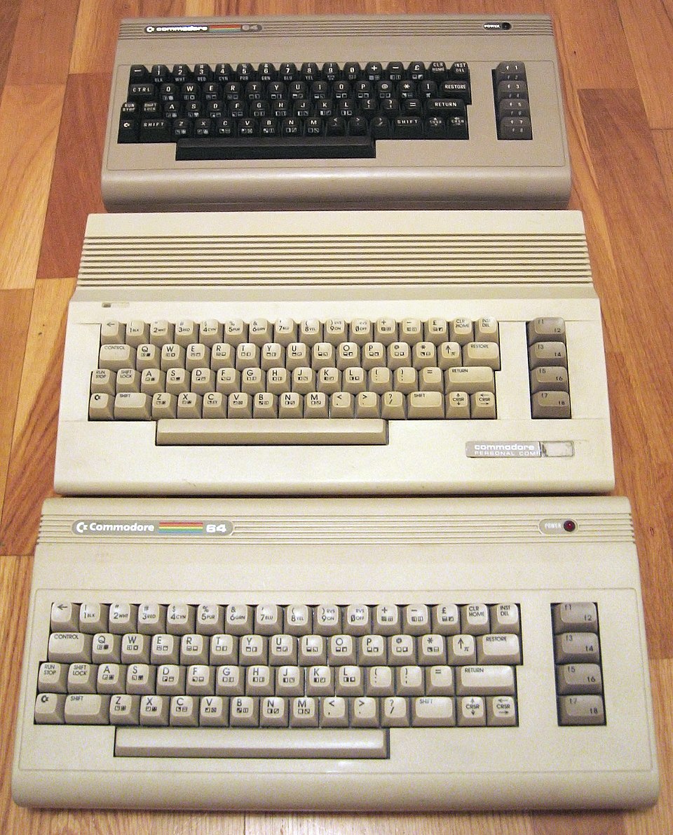 Three Commodore 64 computers stacked, showing the beige breadbox and later cream-colored cases.