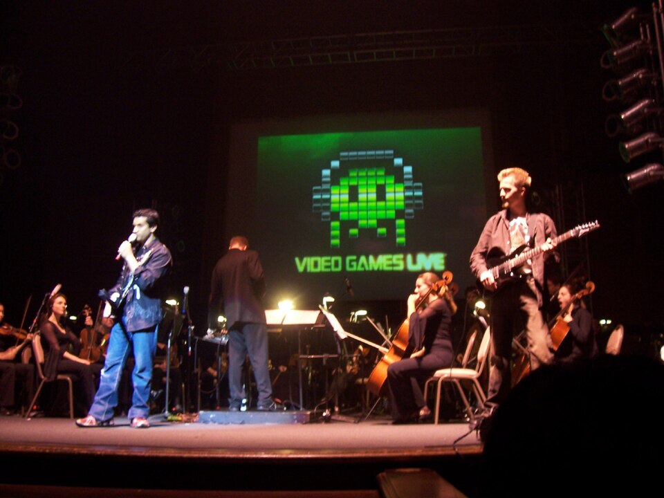 Tommy Tallarico on stage with a guitar addressing the audience at a 2007 concert.