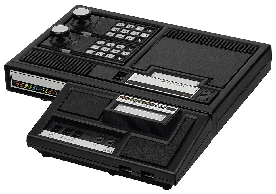 The ColecoVision with a black add-on module attached to its front, carrying Atari-style controller ports.