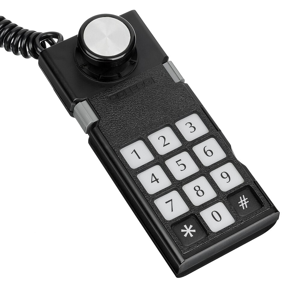 Front view of a rectangular game controller with a 12-key numeric keypad and a stubby joystick.